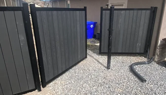 Two gray and black fence gates on a gravel side yard in Utah; both gates are open inward.