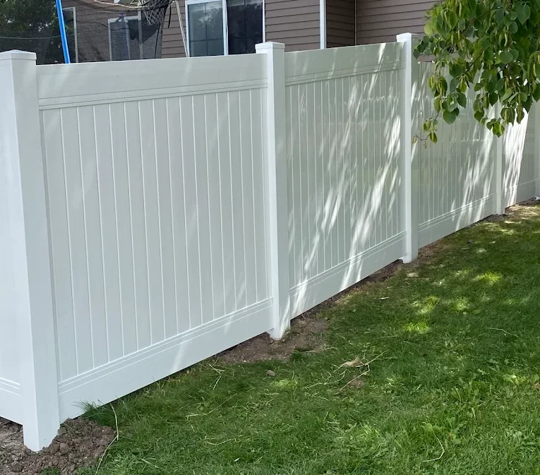 A tall white vinyl privacy fence with vertical panels borders a grassy yard.